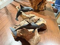Smaller burl wood sculpture with two dolphins in foreground, larger piece behind