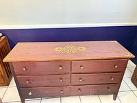 Front view of six-drawer mahogany-tone dresser with yellow stenciling and knobs