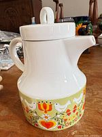Front view of porcelain teapot showing floral and bird motif, lid, handle, and spout