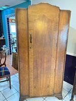Front view of solid wood armoire showing single door, decorative pull, keyhole, medium brown finish