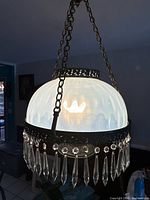 Overall view of chandelier illuminated showing glass shade, metal band, and crystal drops