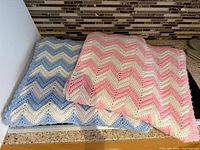 Both chevron blankets folded; blue-white and pink-white-cream colors visible