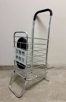 full view of silver aluminum foldable shopping cart with handle extended and one wheel attached
