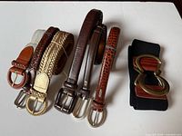 Seven belts laid out showing variety of materials, colors and buckles