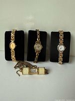 Front view of three gold-tone wristwatches and one cylindrical sliding-cover pendant watch