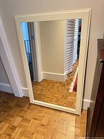 Full view of rectangular cream framed mirror leaning against wall