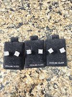 Front view of three pairs of square CZ sterling silver stud earrings on black cards