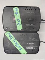 Top view of two APC Back-UPS ES units showing outlet layout, model text, attached power cords and tape notes