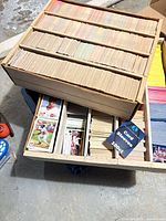 Two large cardboard boxes filled with rows of baseball cards; visible brands and colors; sealed card sleeve pack included