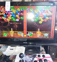 Toshiba TV displaying bubble puzzle game with arcade joystick console in foreground