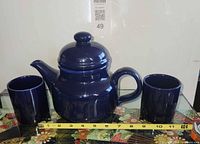 Front view of teapot with lid and two mugs, tape measure for scale