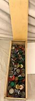 Open wooden box filled with assorted bottle caps