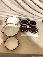Top view of three orange enamel pans and two brown soup bowls with lids