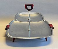 front view showing two chrome tiers, red Bakelite handle, side handles and legs