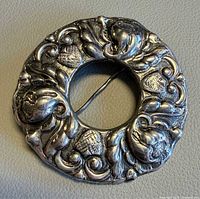 Front view of ornate circular brooch with acorn and leaf design