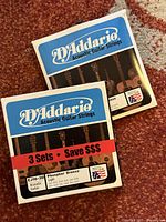 Two blue boxes of D'Addario EJ16-3D light acoustic guitar strings showing fronts and labels