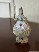 Front view of porcelain lady figurine showing lace skirt, floral decals, hanging loop