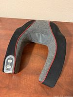 Top view of U-shaped HoMedics neck massager showing grey and black fabric, red piping, and control pad