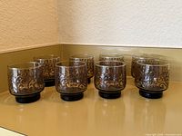 Eight smoke-tone tumblers on countertop showing scroll design and black bases