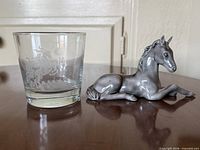 Glass tumbler and metal foal figurine on table