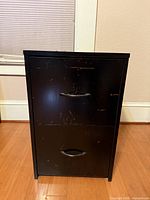 front view of black two-drawer cabinet showing handles and surface wear