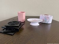 All items grouped: pink tumbler, black coasters stack, ceramic pedestal soap dish, ceramic toothbrush holder