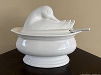 Side view of assembled white ceramic duck-form tureen with ladle