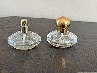 Two clear round perfume bottles with gold spray tops