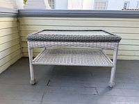 full view of white wicker glass-top table showing glass surface, lower shelf, and legs