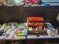 table overview showing open tackle box, clear tackle case, reel and various packaged lures