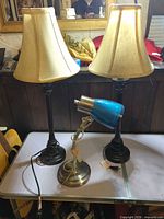 Two tall table lamps with shades and one blue desk lamp arranged on table