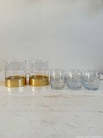 Front view of all six Crown Royal glasses: two gold-base rocks tumblers and four etched shot glasses