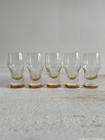 Front view of five shot glasses showing clear bodies and colored bases