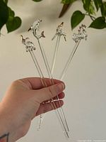 Four clear glass stir sticks held in hand showing animal tops