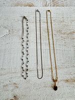 Three necklaces laid flat: bead station chain, snake chain, gold-tone pendant chain