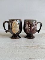 Front view of both pedestal mugs showing leaf motifs and handles