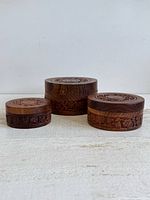 Three wooden boxes with lids on, side view showing carving and size progression