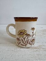 Front view of cream mug with yellow daisy pattern and brown rim