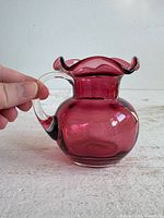 Side view of cranberry glass vase showing ruffled rim and handle