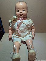 Full view of Reliable composition baby doll seated, showing original clothing and overall condition