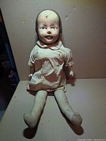 Full view of Dee & Cee composition doll seated, showing cloth body and dress