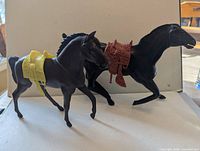 Two black horses with yellow and reddish-brown saddles