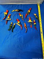 All twelve hand carved wooden parrots displayed on blue background beside measuring tape showing scale
