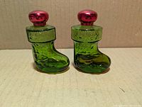 Front view of both green glass stocking-shaped bottles with red caps