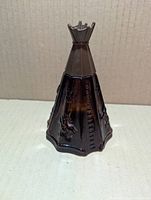 Front view of brown glass teepee-shaped bottle showing raised design
