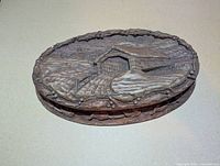 Closed oval trinket box showing covered bridge relief and vine border