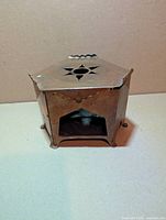 Front view showing arched firebox opening, star vent on hexagonal lid, hammered copper body, three feet