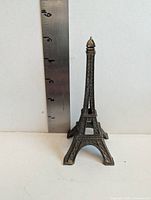 Front view of cast metal Eiffel Tower figurine against ruler showing approximate 5 inch height