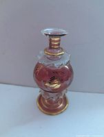 Front view of cranberry glass perfume bottle showing etched floral design and gold gilt accents