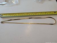 Full view of gold-tone herringbone chain alongside measuring tape confirming 24" length